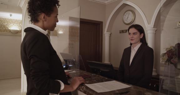 微笑的黑人女性客人在酒店登记入住时听接待员说话