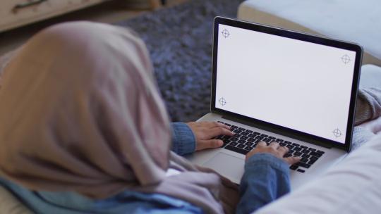 戴头巾的混血女人在家用笔记本电脑工作，在屏幕上复制空间的肩膀视频