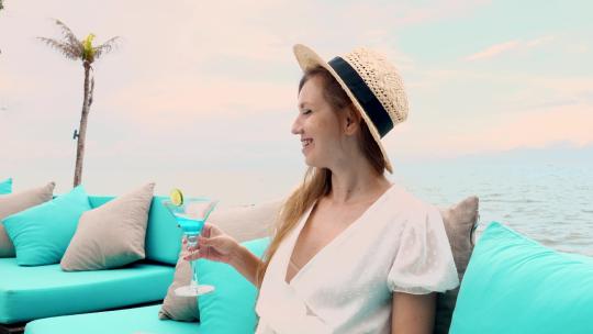 戴着草帽的年轻旅行女子坐在沙发上，享有壮丽的海景