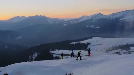 日落时分，一群滑雪旅行徒步旅行者攀登罗尔山口积雪覆盖的山峰。空中