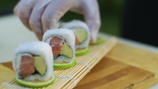 特写镜头中，一名厨师戴着白手套，将美味的寿司卷放在盘子里。慢动作。
