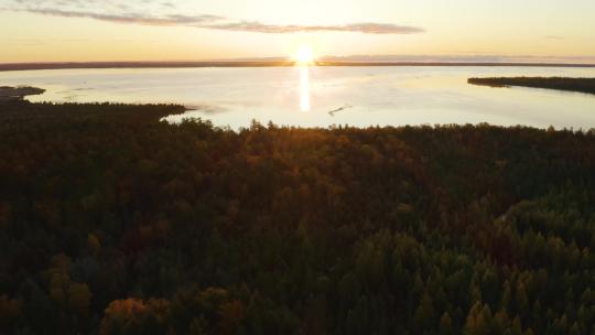 空中，被秋树环绕的偏远湖泊，远处地平线上的日落
