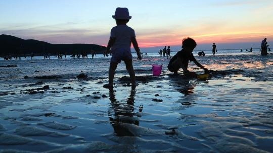 夕阳下海边的儿童正在挖沙子玩耍