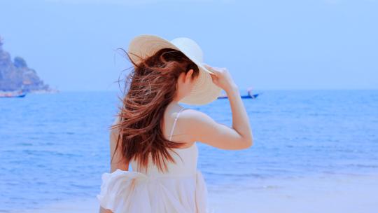 夏季蓝色的海边提着帽子鞋子欢快玩耍的女孩