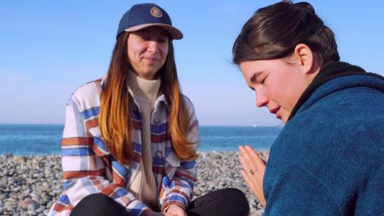 两女子坐在海边的小石头上聊天