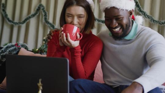 戴着圣诞帽的快乐多样化夫妇微笑着在家打圣诞笔记本电脑视频电话的视频