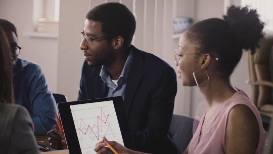 非裔美国商人在办公室会议上交谈、展示手势和交流，看笔记本电脑图表。
