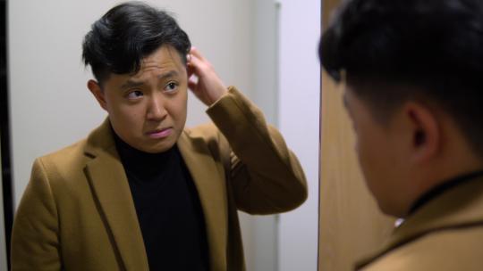 穿着西装的年轻亚洲男子在镜子前整理头发和夹克