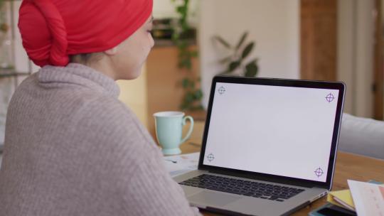 戴头巾的混血儿女人坐在家里的办公桌前，在笔记本电脑上工作，在屏幕上复制空间的视频