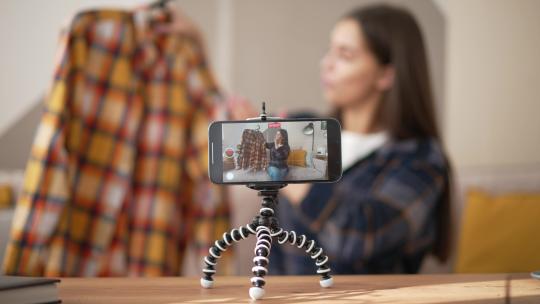 女博主在智能手机上拍摄谈论衬衫的视频。时尚vlogger网红达人为vlog评论休闲衬衫。女孩造型师为她的频道拍摄vlog集。