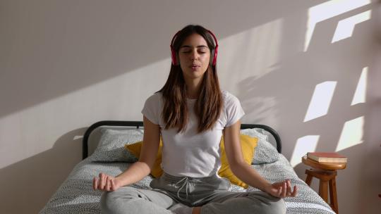 戴耳机呼吸的年轻女子在床上冥想听音乐放松