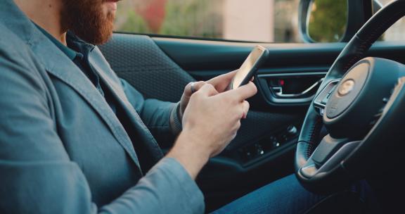 特写商人使用和打字智能手机，在车里手持拍摄。技术概念。未知的男性专业人士在车里用电话聊天。