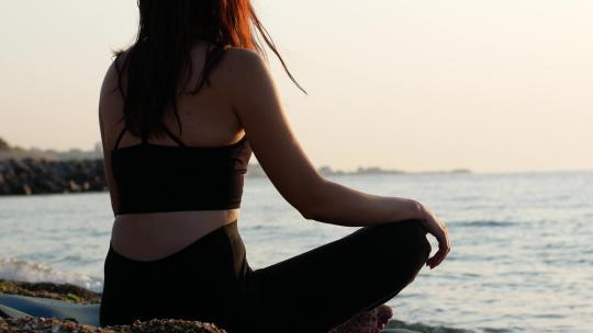 一名瑜伽女子坐在海边的莲花位置，看着太阳黎明的大海