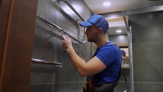 一名水管工和一名穿制服的工人正在用扳手修理浴室墙上的毛巾架