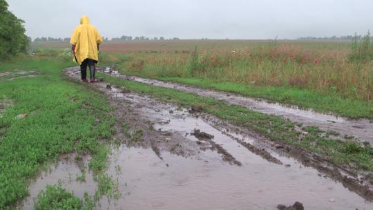 下雨天披着雨衣的男人行走在乡间小路上
