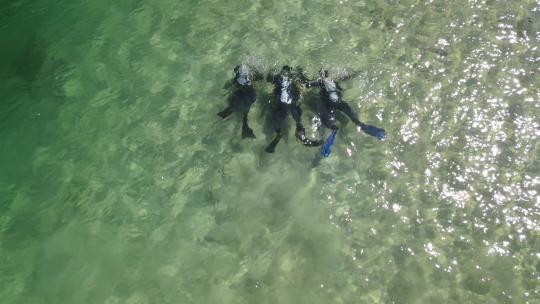 三名水肺潜水员在高山湖边用绿松石水潜水