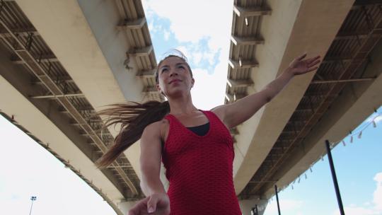 一名穿着红色训练服的成年女子在桥下展示简单的练习